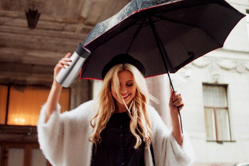Lächelnde Frau mit Regenschirm und To-Go-Becher in der Hand